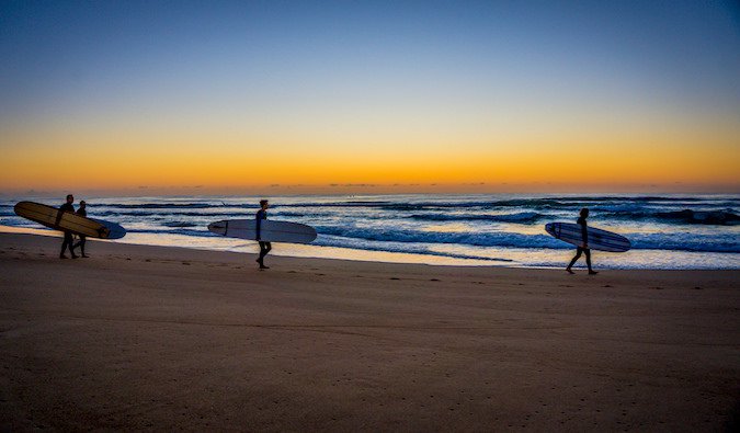 Surfers walking down the beach at sunset with their surfboards