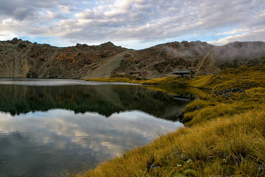 A backcountry hut sits in a basin next to a large alpine lake.
