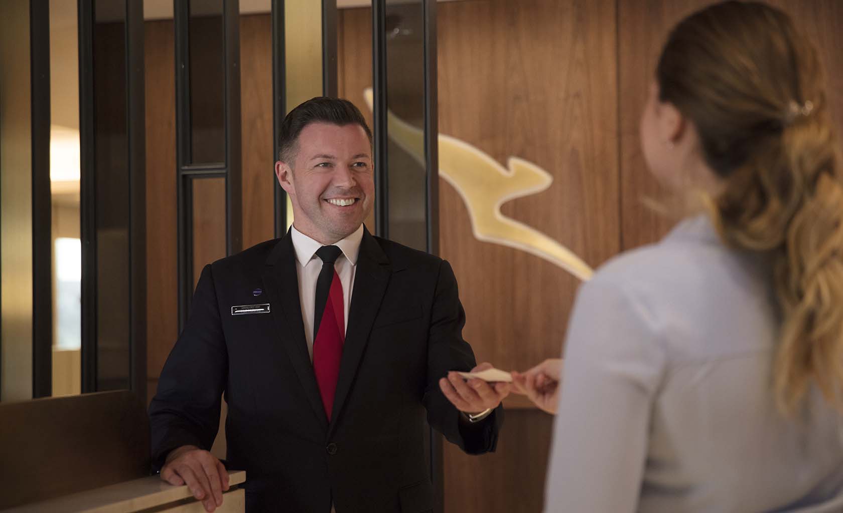 Passenger handing over boarding pass to a Qantas staff member at the reception of the Qantas business lounge in London